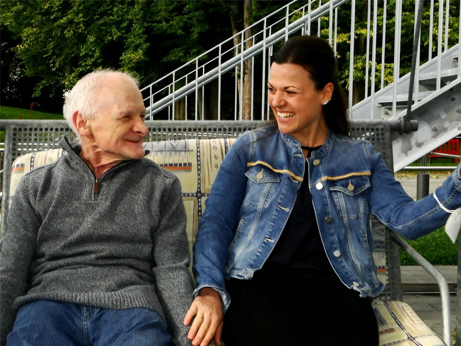 Eine Mitarbeiterin sitzt mit einem Bewohner auf der Schaukel.