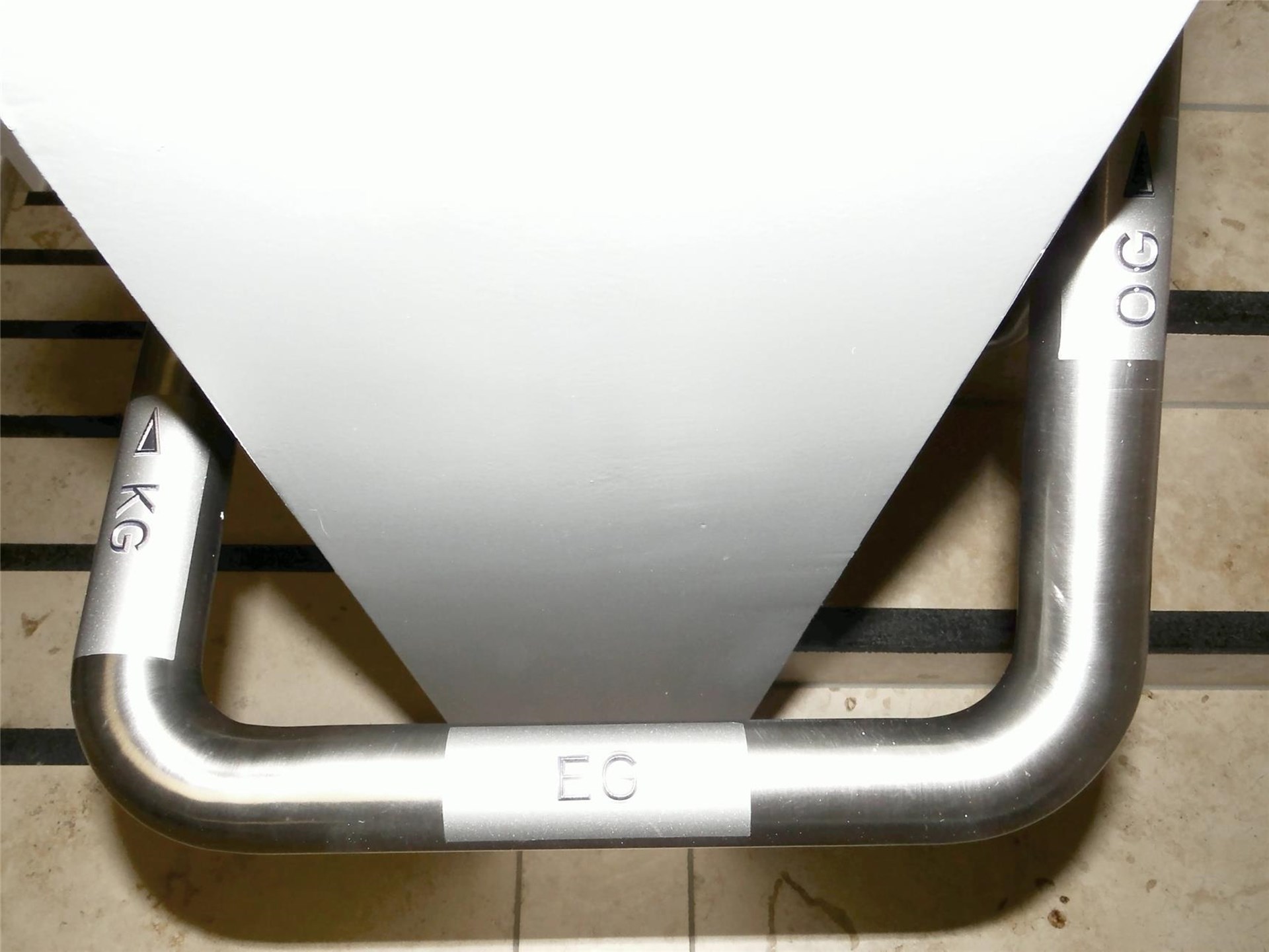 Wir sehen an einer schmalen Wand am Treppenpotest einen Handlauf, der um die Ecken führt. Im ihm sind die Abkürzungen der Etagen eingraviert.